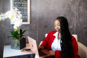 Felicia L Rutledge, PhD in a white button up shirt amd red cardigan sitting at her laptop smiling and typing.